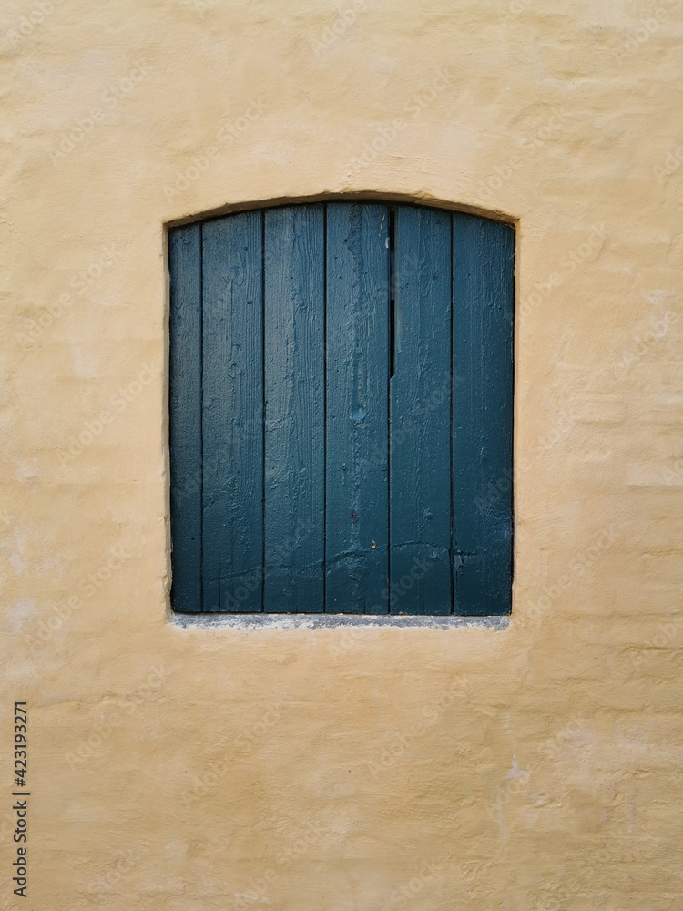 old green closed window with shutters in a yellow wall old green closed window with shutters in a yellow wall