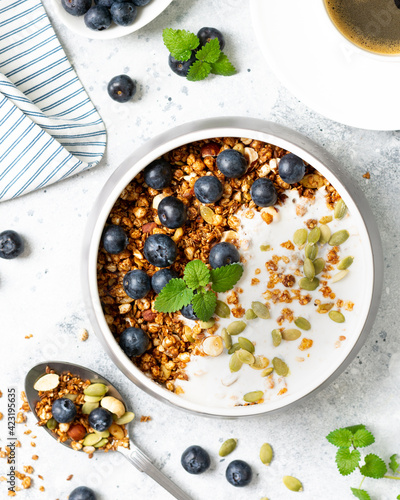 Homemade organic buckwheat granola with yogurt, blueberries, hazelnuts, peanuts, nutmeg, pumpkin seeds and flax seeds in a ceramic bowl on a light background. Breakfast for healthy top view