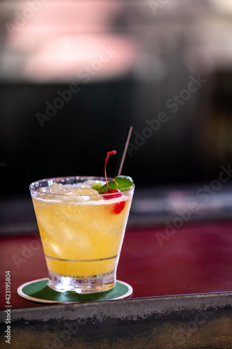 Yellow alcohol cocktail with red cherry served in bar counter