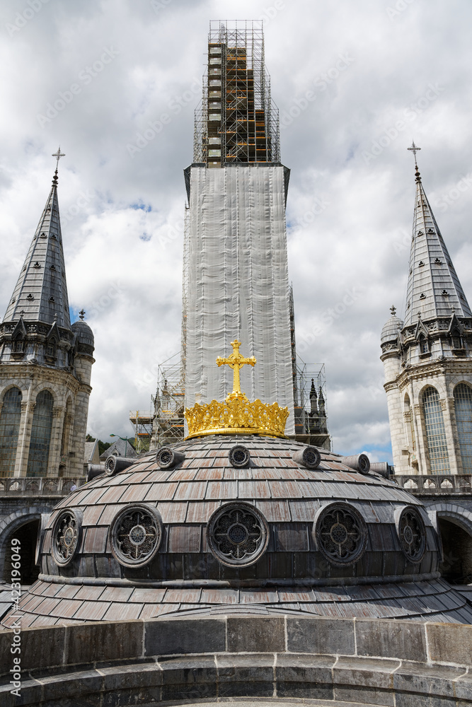 Fototapeta premium Lourdes, France - 22nd august 2020 : Detail of the golden cross on the dome of the basilica of the holy city of Lourdes in front of the work on the main bell tower. Central symmetry