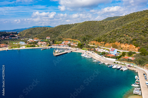 European country village on Mediterranean sea shore with coastline pier for fishing boats. Small resort town with holiday villas along green forest hills summer background