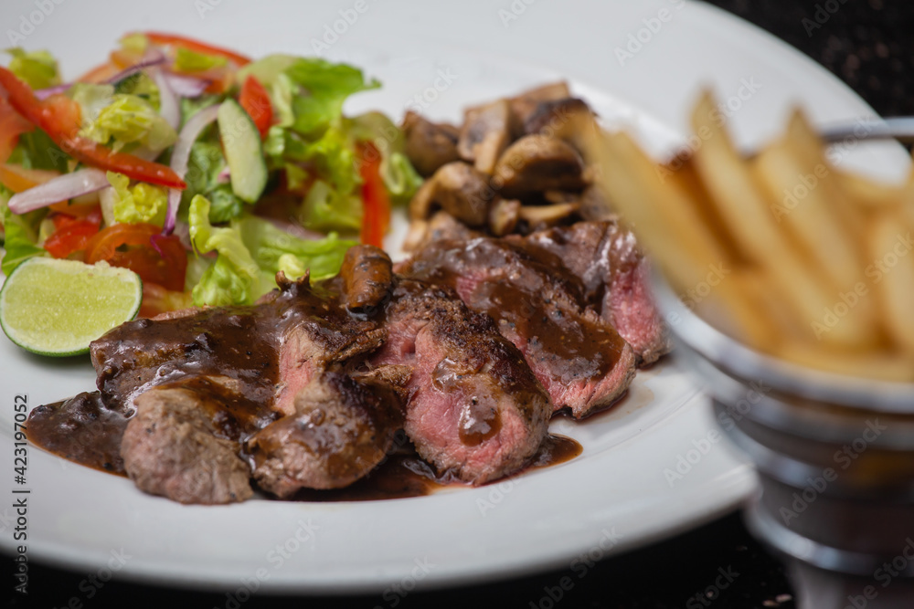 Juicy beef tenderloin steak sliced on a plate with vegetable salad and french frie potatoes