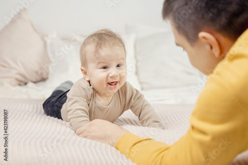 Young father is playing with newborn baby on bed. Dad and son concept