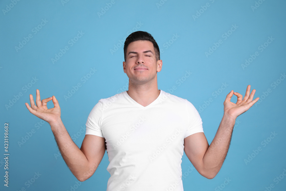 Fototapeta premium Man meditating on light blue background. Stress relief exercise