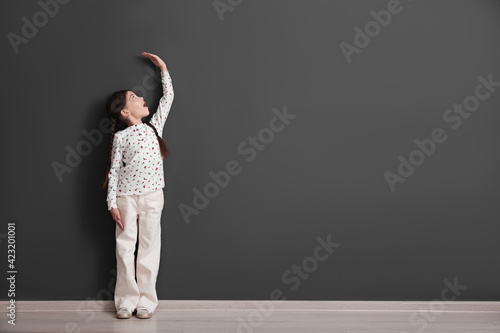 Foto Emotional little child measuring her height near black wall indoors, space for t