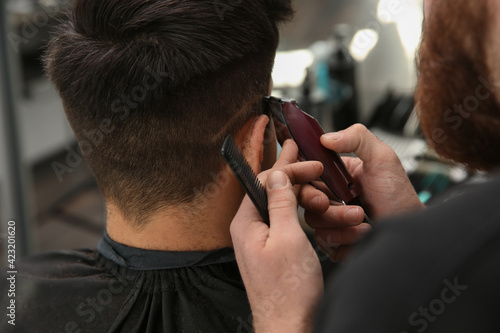 Professional barber making stylish haircut in salon, closeup