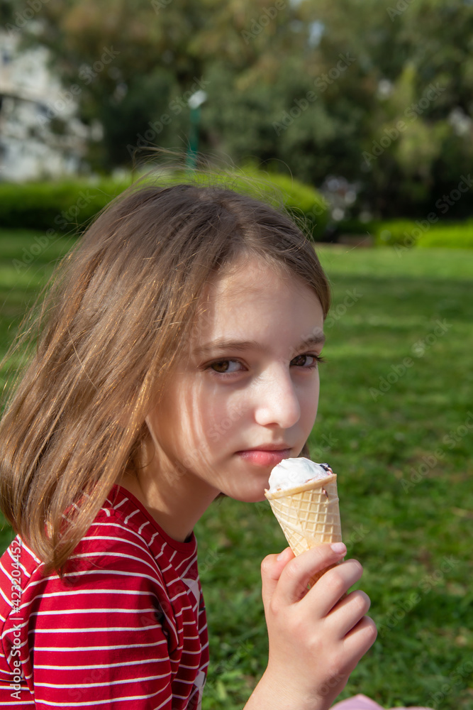 portrait of a thoughtful cute happy beautiful natural teenage girl in a red striped t-shirt with ice-cream against the greenery on a sunny day