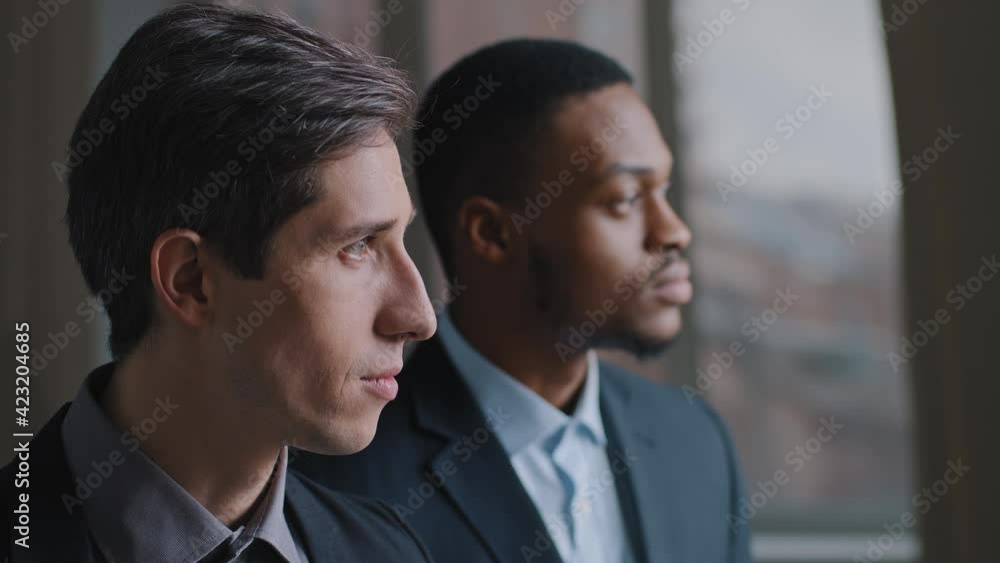 Portrait of two multiracial business men human stand in profile in modern office, Caucasian boss and African American man employee look out window pensive thinking about problem of company planning Portrait of two multiracial business men human stand in profile in modern office, Caucasian boss and African American man employee look out window pensive thinking about problem of company planning