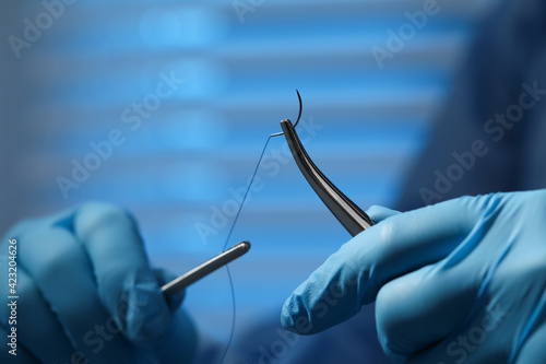 Fotografiet Professional surgeon holding forceps with suture thread on blurred background, closeup
