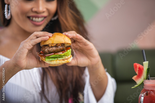 Close up of young woman in casual white clothes eating burger in cafe or restaurant