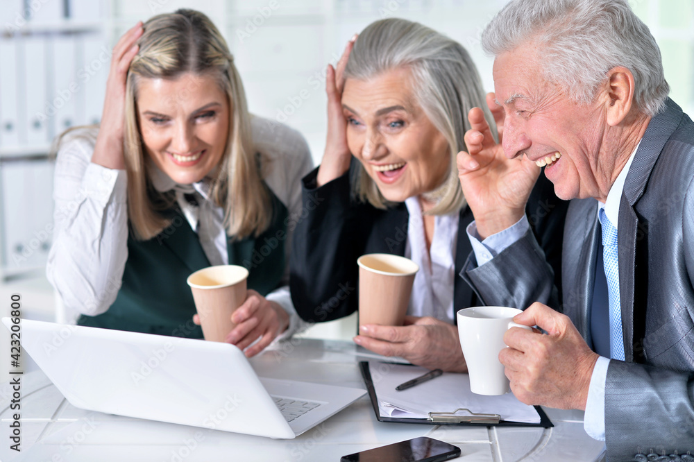 three mature businesspeople using laptop and drinking coffee three mature businesspeople using laptop and drinking coffee