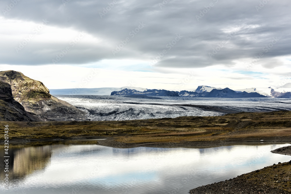 Glacier sloping down to the lake and mountainous terrain in the background. Cold majestic landscape. Iceland.
