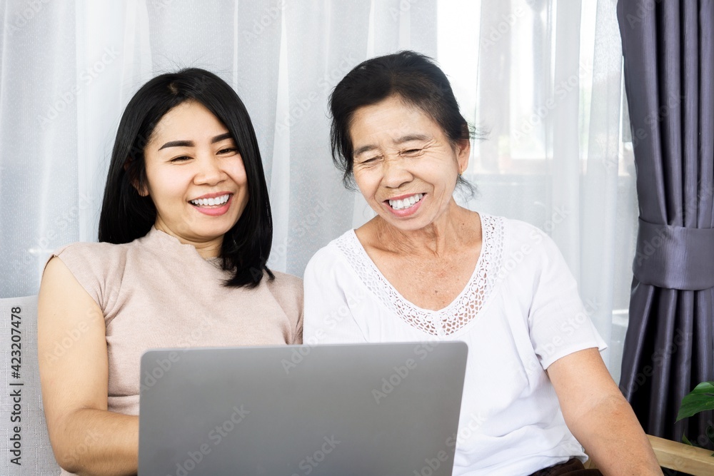Asian daughter showing and teaching her old mother using computer laptop browsing technology on internet Asian daughter showing and teaching her old mother using computer laptop browsing technology on internet