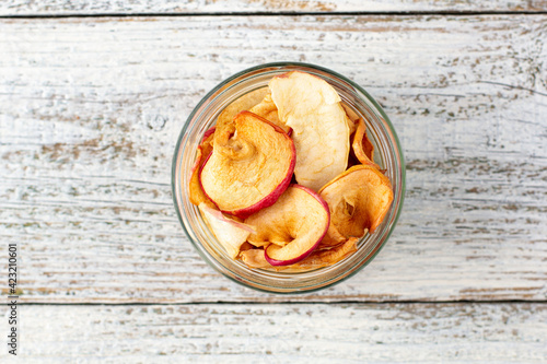 A pile of dried slices of apples in glass jar on white wooden background. Dried fruit chips. Healthy food