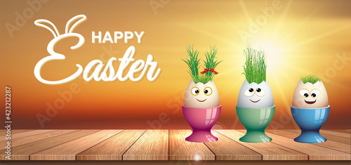 card or banner on Happy Easter in white represented by 3 funny eggs put in their egg cup placed on a wooden floor and in the background the sunset
