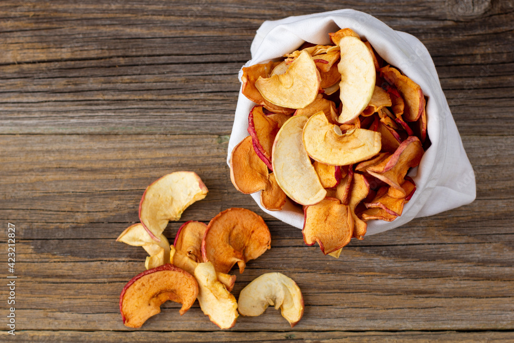 A pile of dried slices of apples pills out of a white pouch on wooden background. Dried fruit chips. Healthy food A pile of dried slices of apples pills out of a white pouch on wooden background. Dried fruit chips. Healthy food