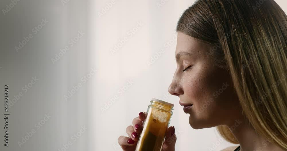 Casual young woman cooking in kitchen choosing spice to add to the dish. Housewife holding a small glass jar with turmeric, enjoying pleasant smell. Casual young woman cooking in kitchen choosing spice to add to the dish. Housewife holding a small glass jar with turmeric, enjoying pleasant smell.