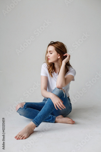 young caucasian woman posing in t-shirt, ripped jeans, sitting on studio floor