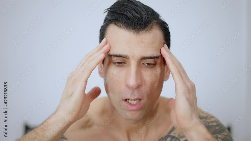 Headshot of young overwhelmed man rubbing temples looking at camera with brown eyes. Close-up portrait of tired Middle Eastern guy having migraine in bedroom at home. Headache and stress. Headshot of young overwhelmed man rubbing temples looking at camera with brown eyes. Close-up portrait of tired Middle Eastern guy having migraine in bedroom at home. Headache and stress.
