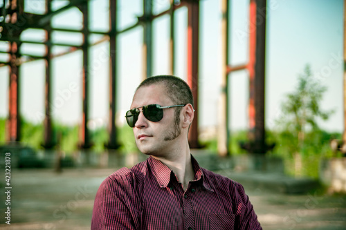 A man in a plaid shirt and sunglasses with sideburns in an abandoned building for demolition walks in military boots