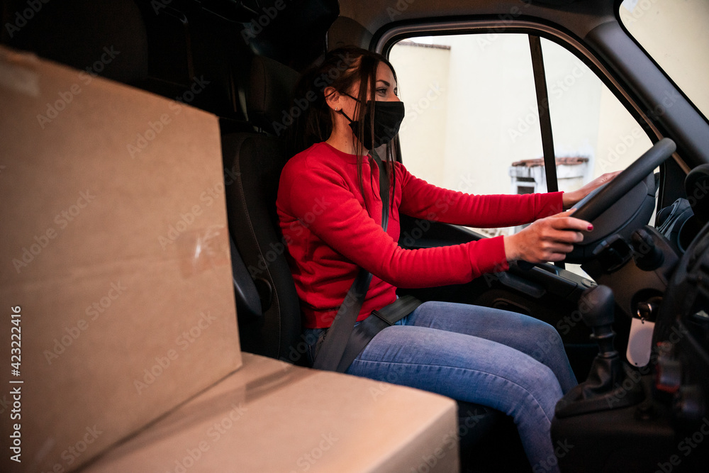 Young courier woman sitting in her van drives to customer parcel delivery destinations during the global pandemic from Coronavirus Covid-19 - Concept of safe shipments