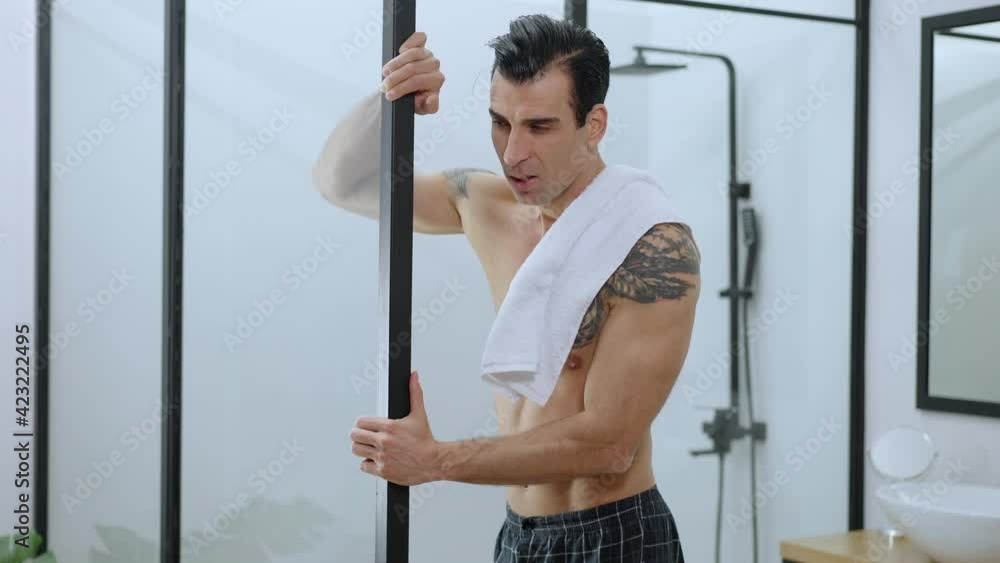 Refreshed man standing at shower with white towel on shoulder smiling. Middle shot portrait of satisfied Middle Eastern handsome guy taking care of body in bathroom in the morning. Daily routine. Refreshed man standing at shower with white towel on shoulder smiling. Middle shot portrait of satisfied Middle Eastern handsome guy taking care of body in bathroom in the morning. Daily routine.