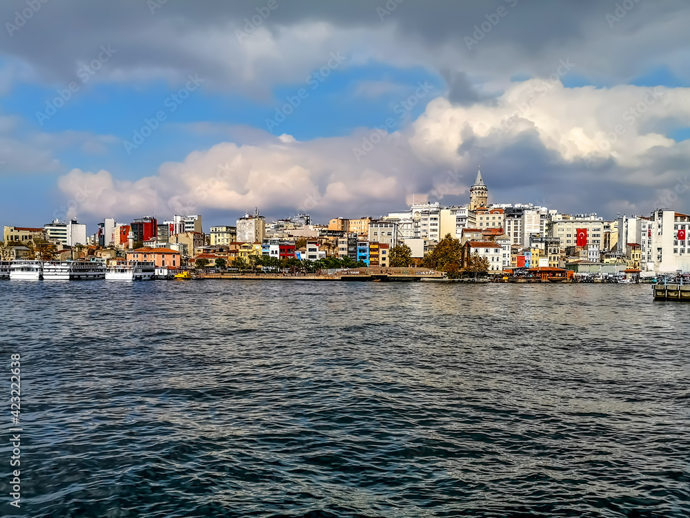 Istanbul, Turkey - October 29, 2019: View from the sea to the Karakoy district with Galata Tower against the backdrop of a cloudy sky in Istanbul. City skyline with old colorful buildings on the shore