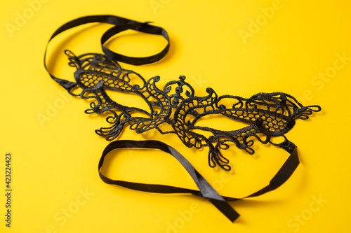 Black lace eye mask on yellow background. Delicate lace mask. Butterfly eyes mask for carnival. Close up