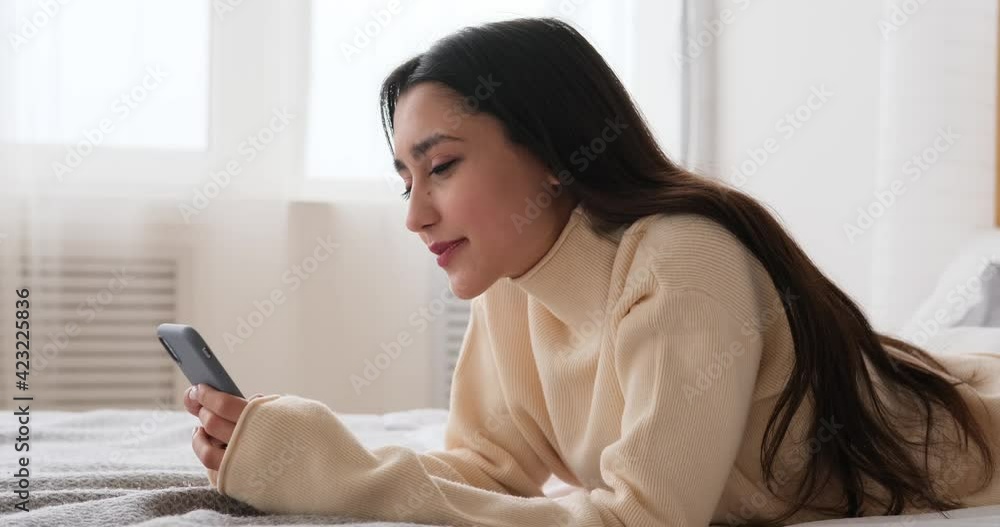Woman laughing while using mobile phone lying on bed at home Woman laughing while using mobile phone lying on bed at home