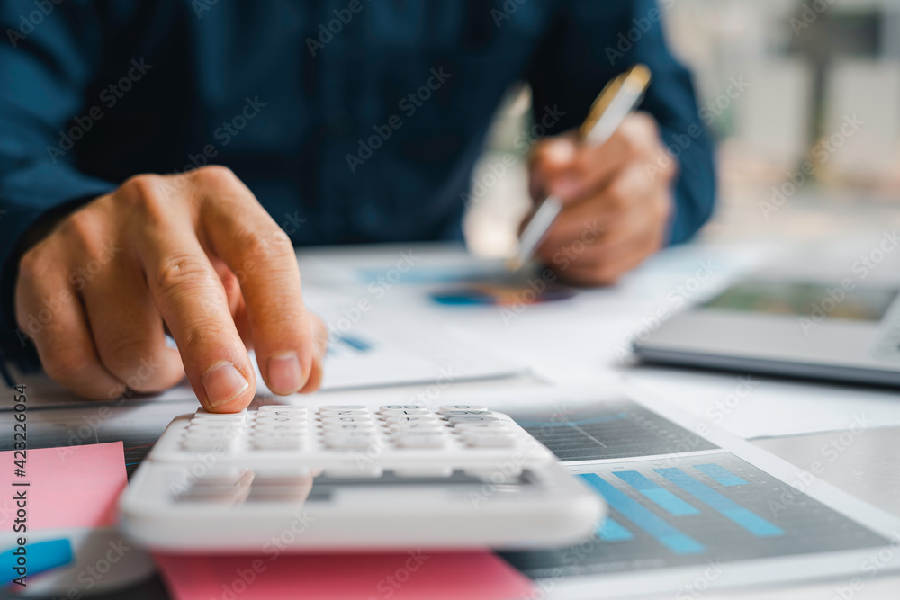 Male accountants or businessmen use a calculator and laptop to calculate investment results. And making financial reports on the desk Business finance accounting concept Male accountants or businessmen use a calculator and laptop to calculate investment results. And making financial reports on the desk Business finance accounting concept