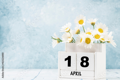 cube calendar for april decorated with daisy flowers over blue with copy space