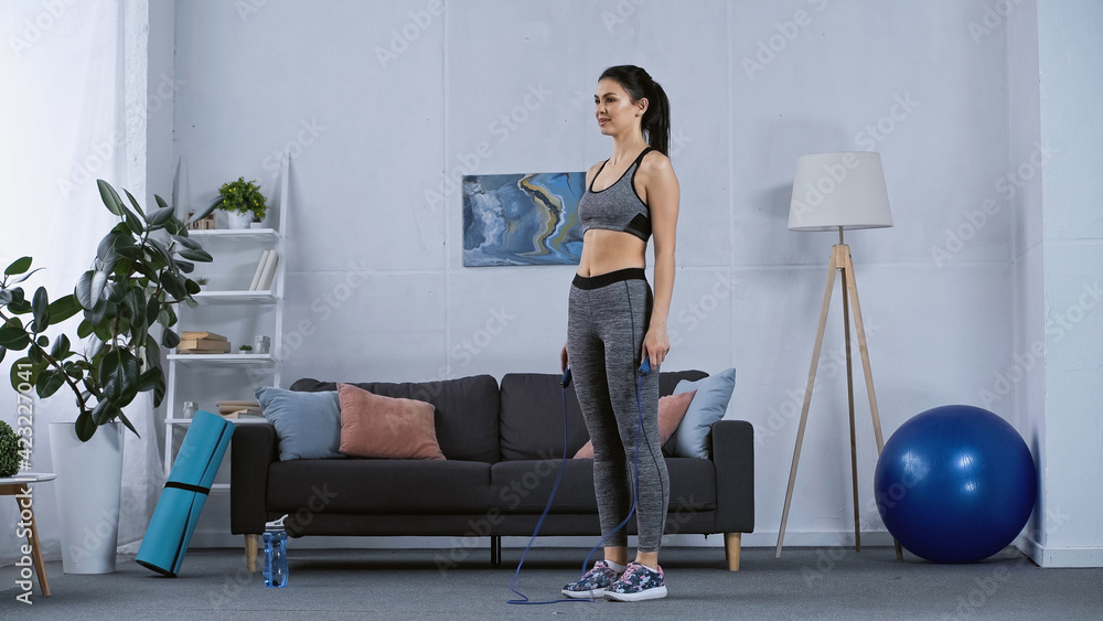 Fototapeta premium young woman in sportswear working out with jumping rope at home