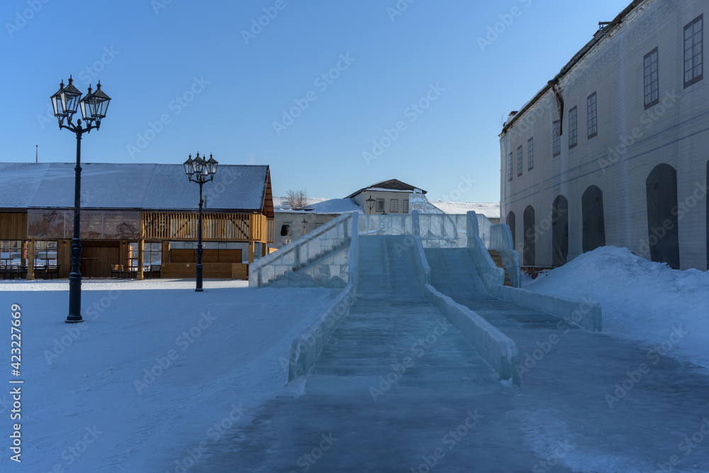 A high ice slide at the Market Square in the city of Tobolsk (Siberia, Russia) on a frosty winter day. A place for entertainment for children on winter days. Historic place in the city, pure snow