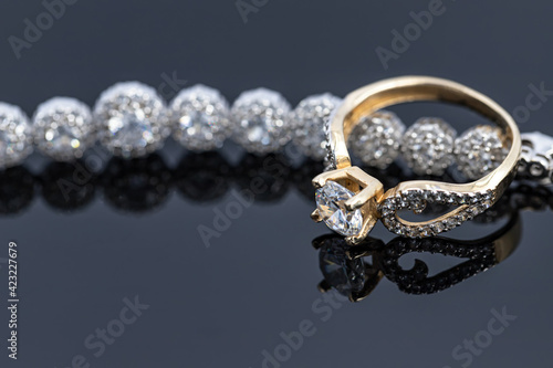 An elegant women's gold ring with a diamond is placed on a bracelet with precious stones