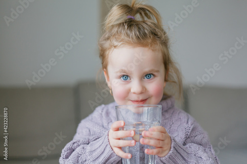 A little girl holds a glass of water, drinks.