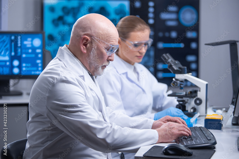 Professor and his young and professional laboratory assistant are doing scientific experiment in a modern laboratory. Genetic engineers workplace. The concept of science, medicine and vaccine. Professor and his young and professional laboratory assistant are doing scientific experiment in a modern laboratory. Genetic engineers workplace. The concept of science, medicine and vaccine.