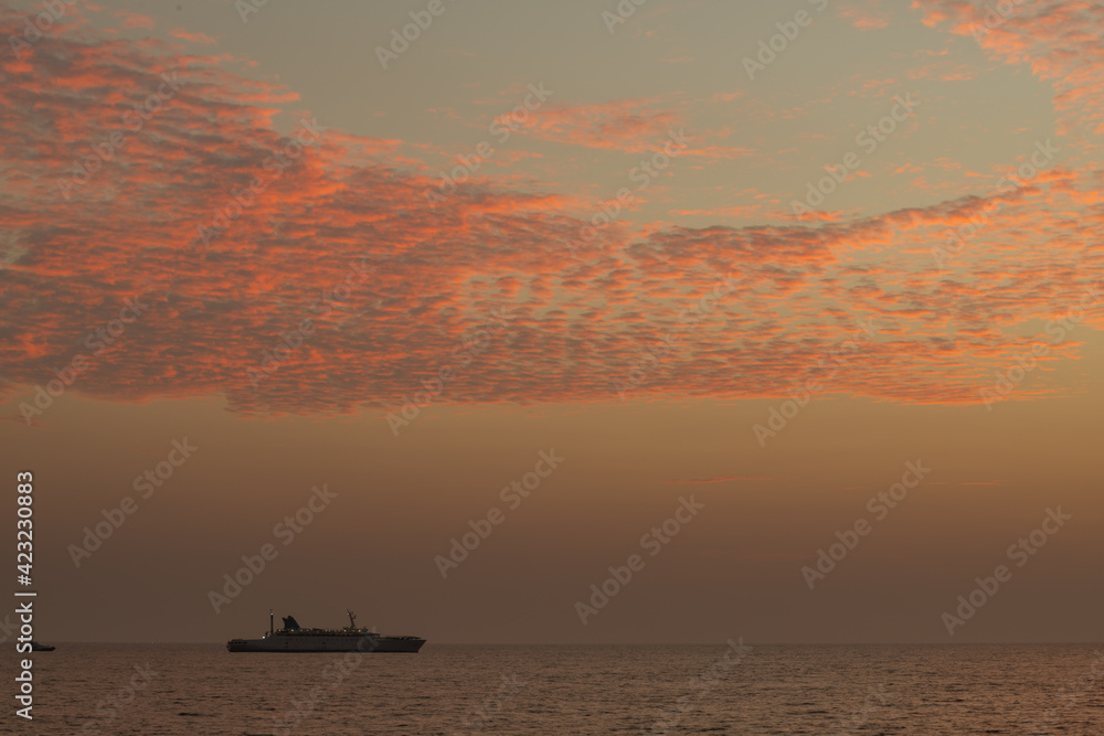 A ship traveling in the horizon, glorious colorful sunset skies, calm low tide ocean shore, view from the famous Galle fort.