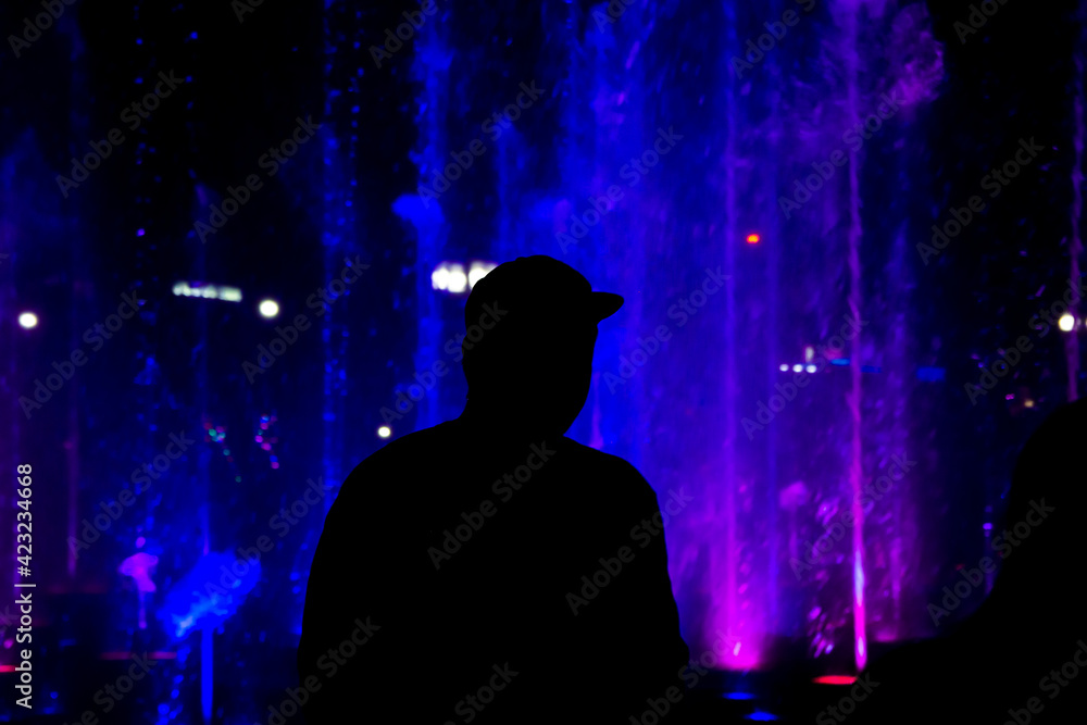 Black Silhouette of a man against the backdrop of a fountain backlit in blue Black Silhouette of a man against the backdrop of a fountain backlit in blue