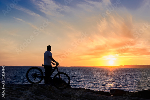 Silueta de un chico mirando el atardecer desde una roca sobre el mar