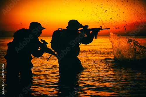 Foto Army soldiers team, special operation forces infantrymen landing on seacoast, aiming and shooting with service rifle during firefight on shore at evening or morning time