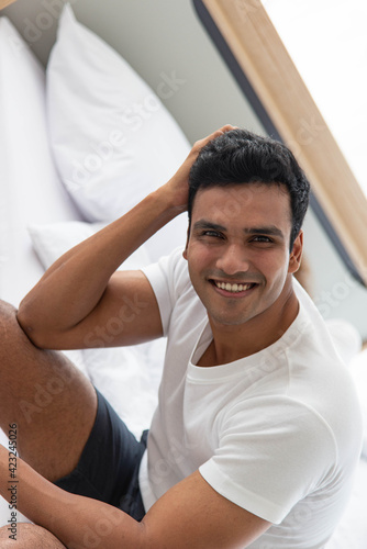 Young smiling Asian man sitting on bed relax in the morning