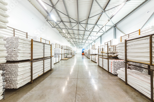 Spacious light interior of a large warehouse in a factory with special racks and shelves and products placed on them.
