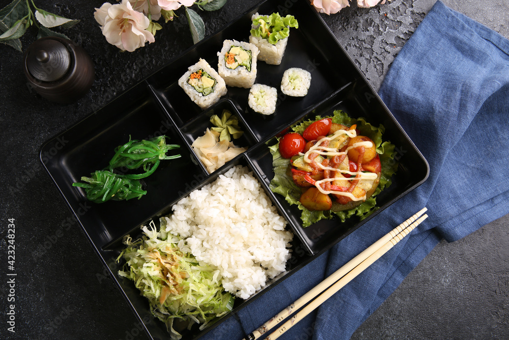 Japanese cuisine. Business lunch in a black box: rice, rolls, salad, sushi on a black table. Background image, copy space