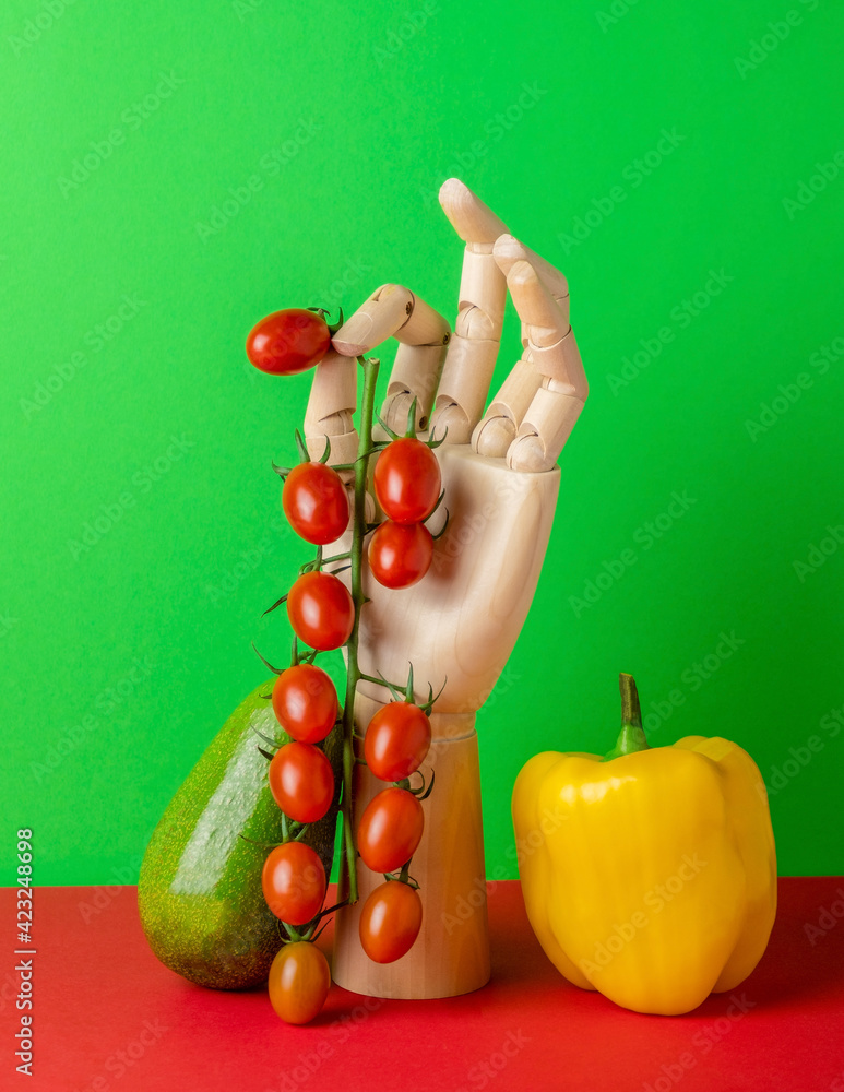 Modern still life with wooden hand and fresh vegetables on a green red background