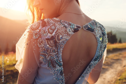 Beautiful bride in blue wedding dress with embroidery and bare back walking in mountains at sunset.