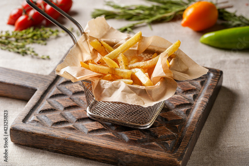 French fries on a wooden chopping board with a beautiful background of vegetables and herbs.