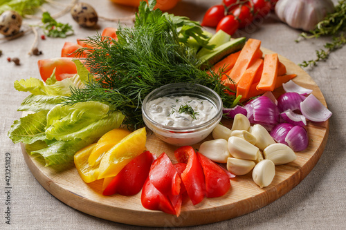 Slicing fresh vegetables from peppers, carrots, cucumbers, garlic, tomatoes, dill, onions, parsley, lettuce leaves on a round wooden board with a beautiful background.