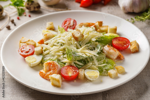 Caesar salad with shrimps  on a large white plate on the table covered with a light linen cloth on a beautiful background of vegetables and herbs. Beautiful bokeh.