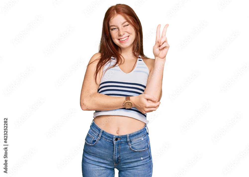 Young read head woman wearing casual clothes smiling with happy face winking at the camera doing victory sign. number two. Young read head woman wearing casual clothes smiling with happy face winking at the camera doing victory sign. number two.
