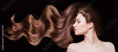 Brown Hair. Beautiful young woman with healthy luxurious long hair on dark background. Hairstyle. Hair cosmetics